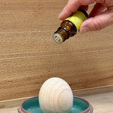 Dropping HONO-KA Yuzu essential oil onto the egg-shaped wood diffuser in a ceramic dish
