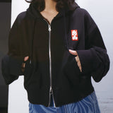 Person wearing a black hoodie with a red and white logo on a plain background