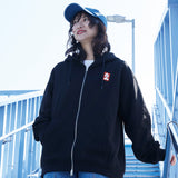 Person wearing a black hoodie with a logo, standing on a bridge.