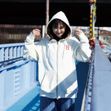 Person wearing a white hoodie with a logo on a bridge