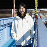 Person wearing a white hoodie with a logo on a bridge