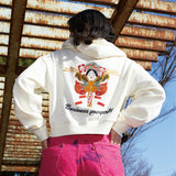 Person wearing a white hoodie with a colorful design and text, standing in front of a rustic wooden wall.