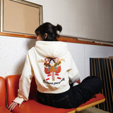 Person wearing a white hoodie with a graphic design sitting on a red chair.